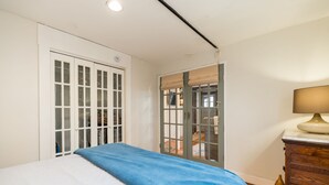 A bedroom with a bed, a dresser, a lamp, and a sliding glass door leading to a balcony.