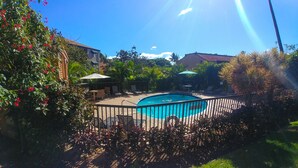 Una piscina rodeada por una valla, con un área de patio y sillas de descanso.