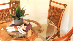 Una mesa redonda de vidrio rodeada de sillas de mimbre, con una planta en maceta y un adorno colgante en la pared.