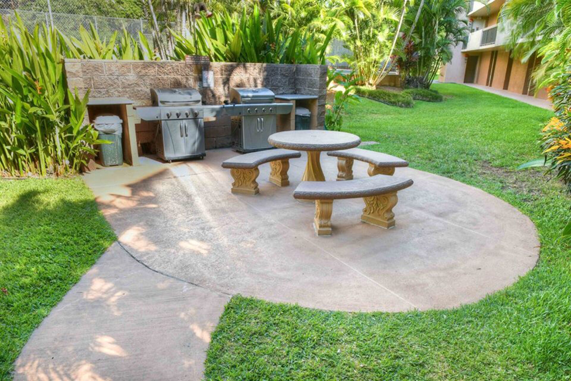 Patio esterno con tavolo e panche in pietra, una griglia e un barbecue.