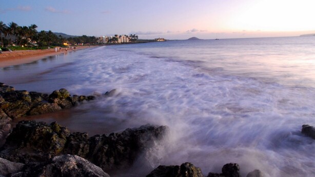 Una playa con costa rocosa y aguas tranquilas.