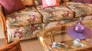 A living room with a floral sofa, a glass coffee table, and a large mirror on the wall. - Family Friendly Condo w/Loft & Steps from Charley Young/Kam 1 Beach (Kihei)