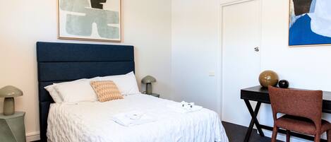 A neatly arranged hotel room with a bed, bedside tables, a desk, and a chair.