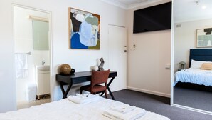 Habitación de hotel con cama, escritorio, silla, un espejo grande y un cuadro en la pared.