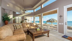 A spacious living room with a large beige sectional sofa, a wooden coffee table, and a view of the ocean through large windows.