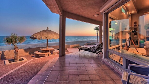 A beachfront patio with a thatched umbrella, lounge chairs, and a telescope.