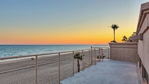 A balcony with a view of the beach and ocean during sunset.