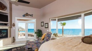A bedroom with a large bed, a TV, a fireplace, and a view of the beach.