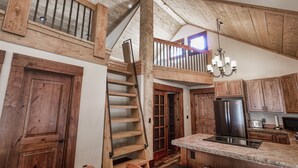 A rustic kitchen with wooden beams, a central island, and a staircase leading to an upper level.