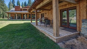 A wooden cabin with a covered patio, outdoor seating, and a stone fireplace.