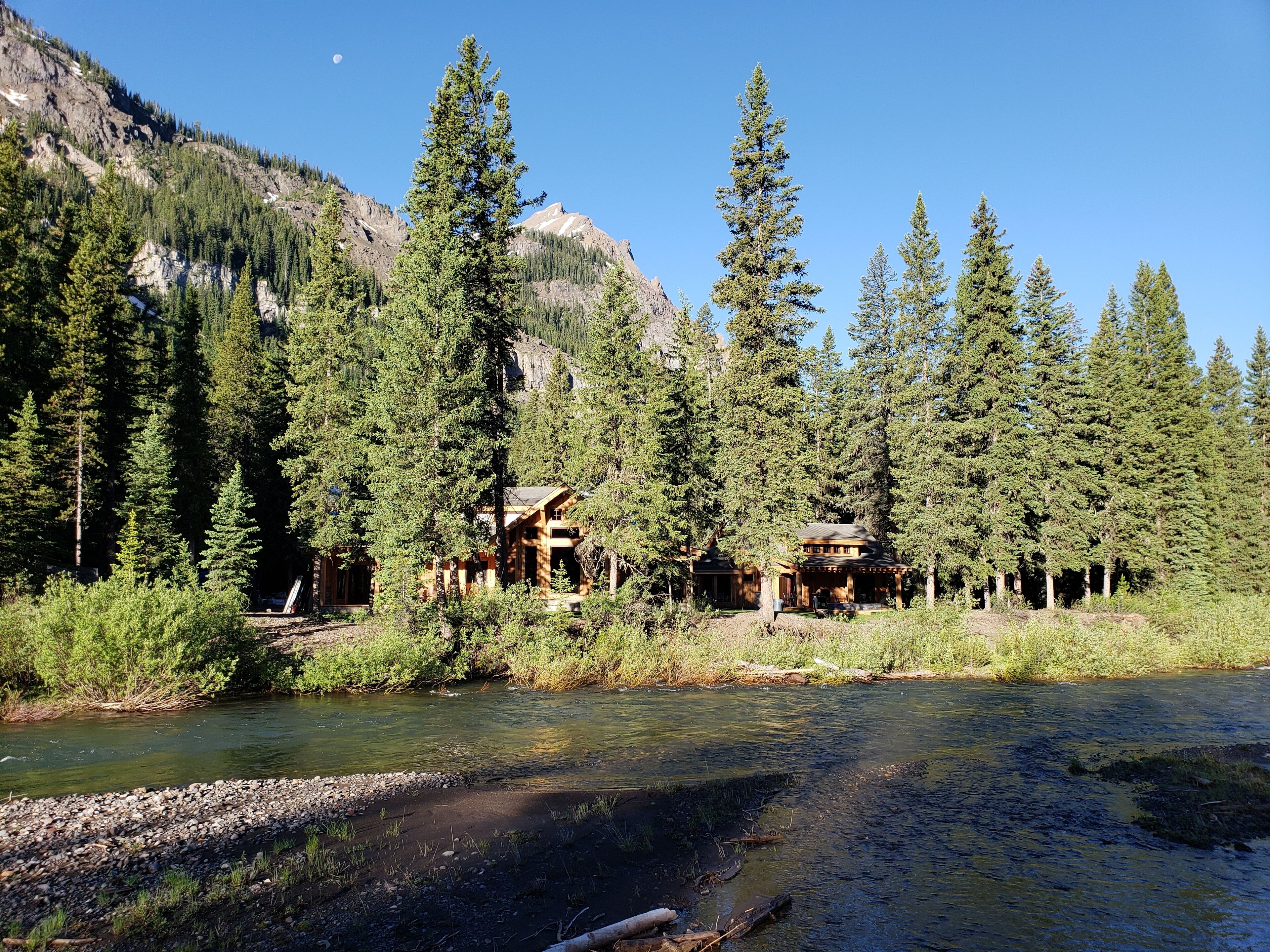 Un chalet au revêtement extérieur en bois, entouré de grands pins et adossé à une montagne.