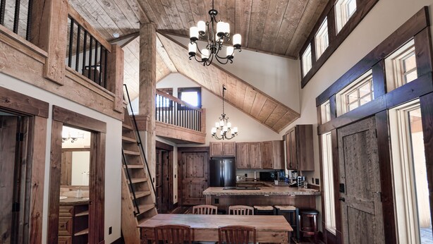 A rustic kitchen with wooden beams, a chandelier, and a dining area with a table and chairs.