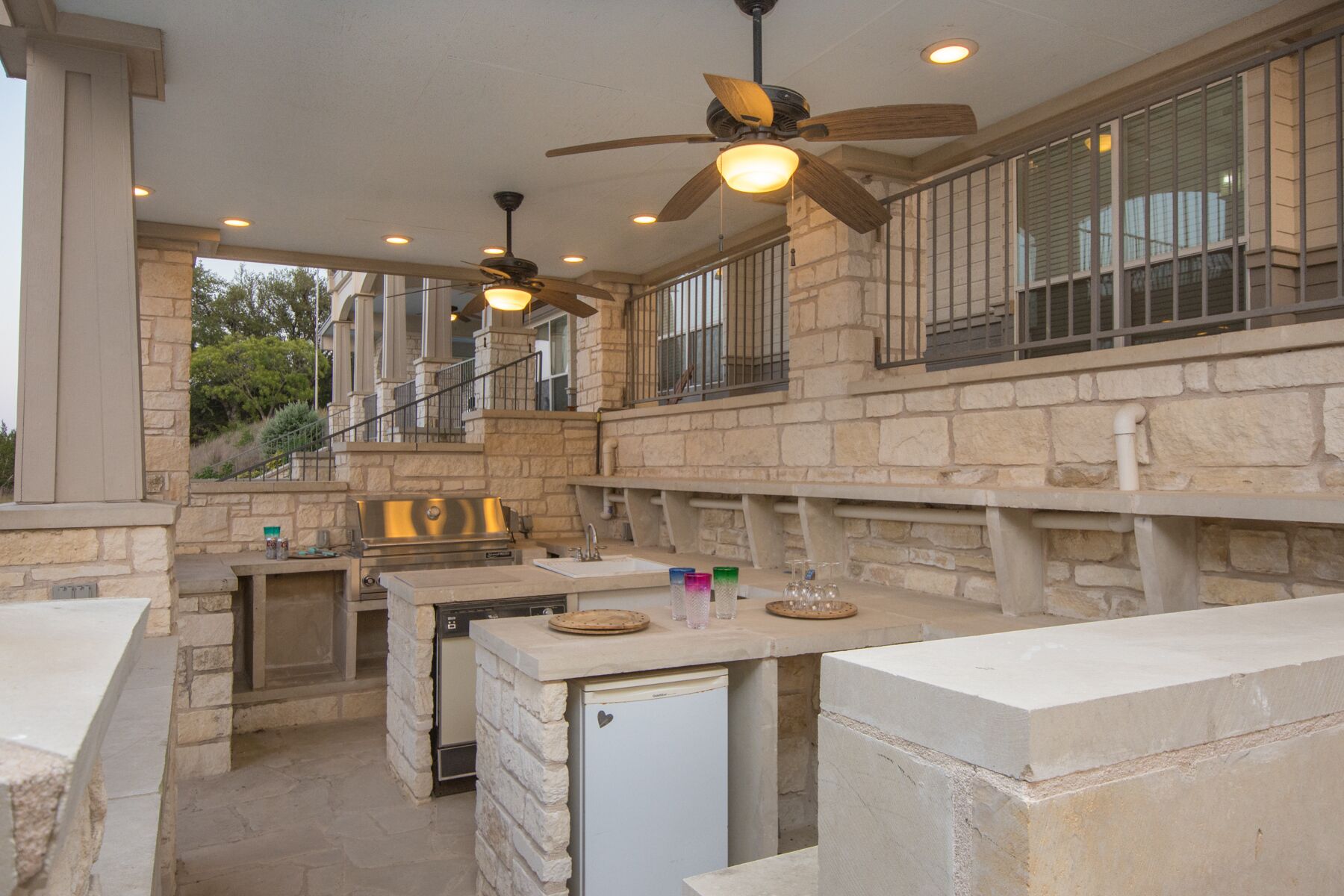 An outdoor kitchen area with stone walls, a built-in grill, and a ceiling fan.