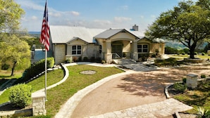 A two-story house with a stone facade, a front porch, and a driveway leading to the entrance. - Gorgeous 4900 square foot pool & spa home minutes from Lake Travis and winery (Marble Falls)