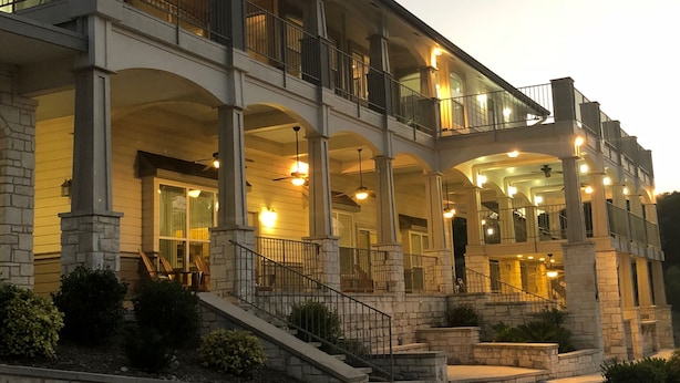 A two-story building with a balcony, stone columns, and a staircase leading to the entrance. - Gorgeous 4900 square foot pool & spa home minutes from Lake Travis and winery (Marble Falls)