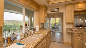 A spacious kitchen with granite countertops, wooden cabinets, and a large window offering a view of the countryside. - Gorgeous 4900 square foot pool & spa home minutes from Lake Travis and winery (Marble Falls)