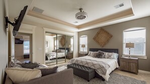 A bedroom with a large bed, a sitting area with a sofa, a mirror, and a ceiling fan. - Gorgeous 4900 square foot pool & spa home minutes from Lake Travis and winery (Marble Falls)