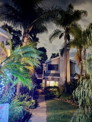 A residential property with a pathway leading to a house, surrounded by lush greenery and palm trees.