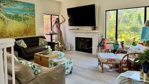 Un salon moderne doté d’une cheminée, d’un téléviseur et de grandes fenêtres offrant une vue sur la verdure.
