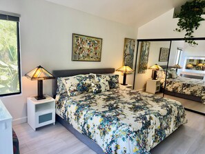 Une chambre à coucher comprenant un lit, deux lampes de chevet, une table de chevet, un miroir et une fenêtre donnant sur un paysage verdoyant.