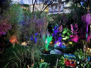 A garden with various plants and trees, some illuminated by colored lights. - 4 Bdrm Private Jungle House, minutes to all, patios, fire pit,  parking, trees! (San Diego)