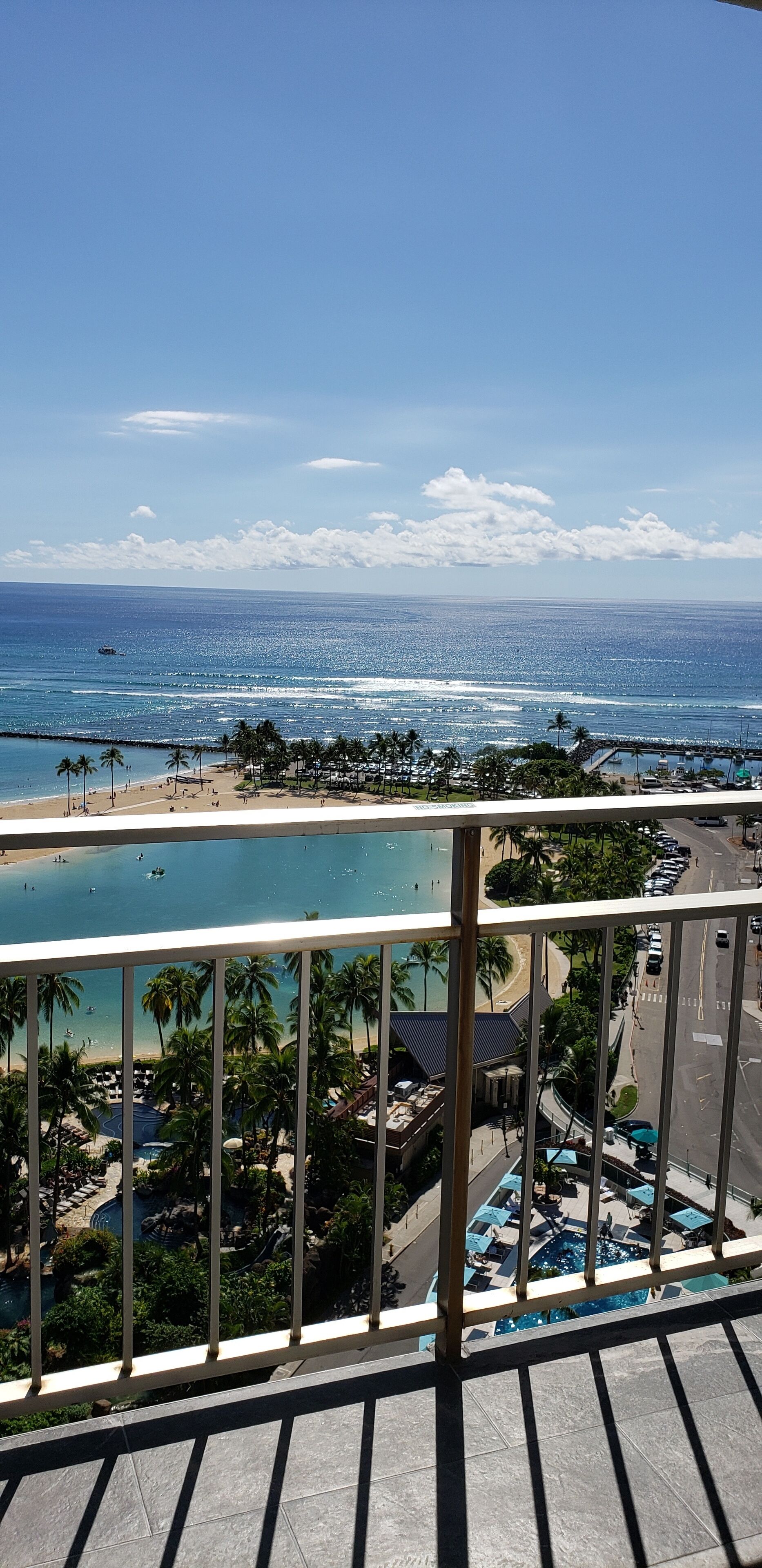 A view from a balcony overlooking a beach with a pool area, palm trees, and a clear sky.