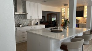 Una cocina moderna con armarios blancos, una isla grande con taburetes de bar y un salpicadero de azulejos en espiga.