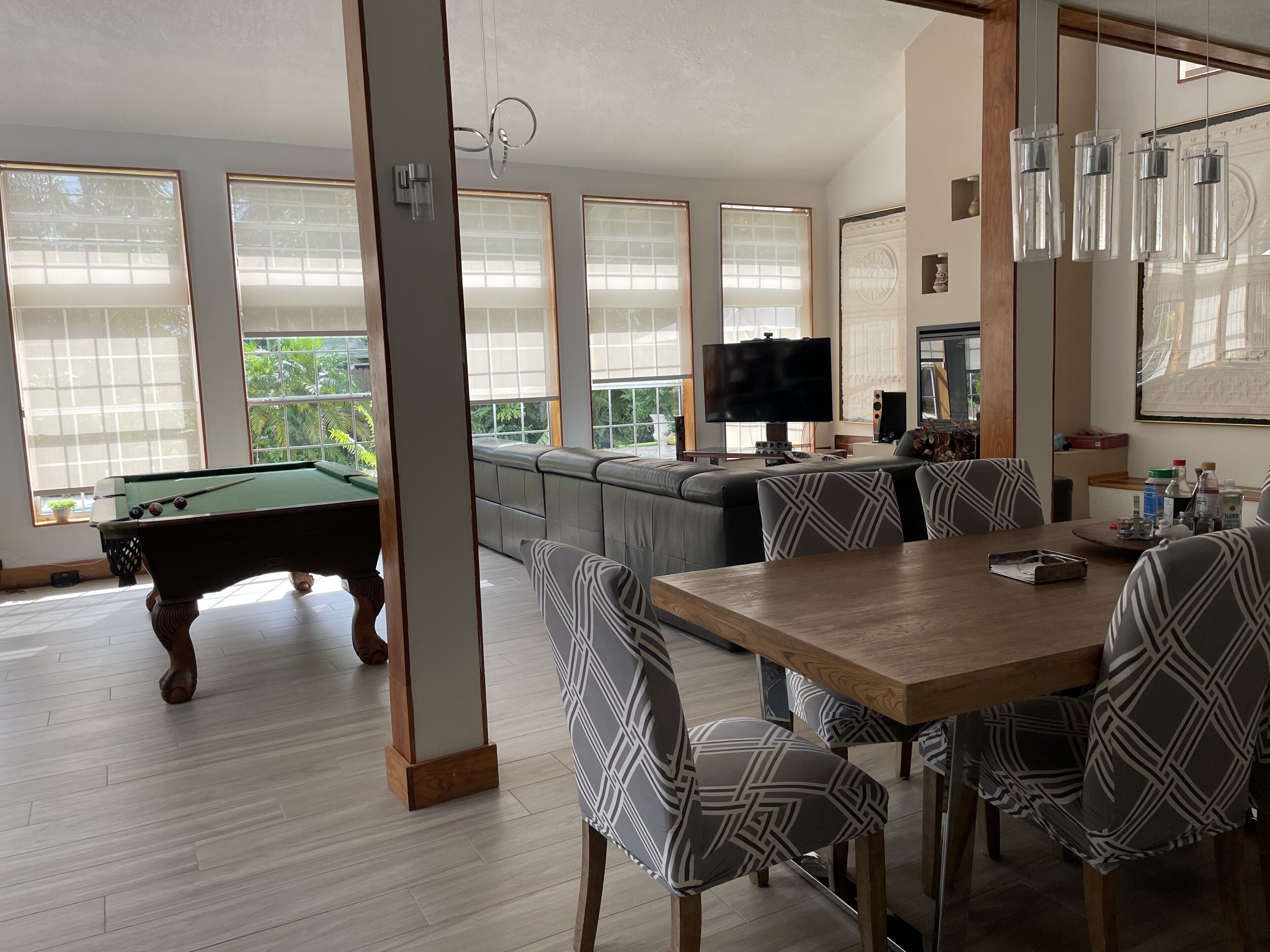 A modern living room with a pool table, a large sectional sofa, and a dining area with patterned chairs.