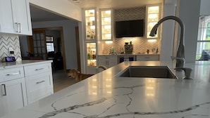 Una cocina moderna con armarios blancos, encimera de mármol y televisión integrada.