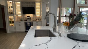 Una cocina moderna con armarios blancos, encimera de mármol y televisión empotrada.