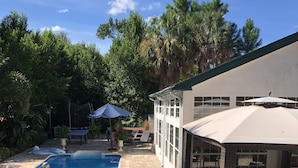 Un patio trasero con piscina, sillas de descanso y un porche cubierto.