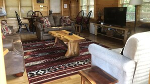 A cozy cabin interior with a wooden floor, a leather sofa, a wooden coffee table, and a television. - Cozy Getaway Long Range View Paved Access Minutes To Downtown Blue Ridge Hot Tub (Blue Ridge)