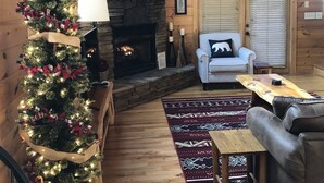 A cozy cabin interior with a stone fireplace, a Christmas tree, a sofa, and a wooden ceiling. - Cozy Getaway Long Range View Paved Access Minutes To Downtown Blue Ridge Hot Tub (Blue Ridge)