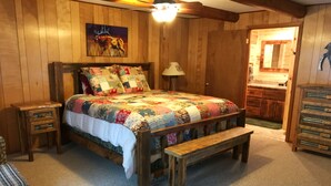Een gezellige slaapkamer met een houten bed, een sprei, een bankje, een nachtkastje, een lamp en een schilderij aan de muur.