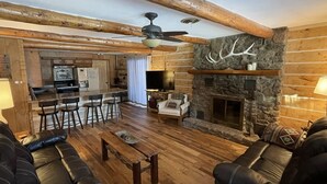 Een landelijke woonkamer met een stenen open haard, houten balken, leren banken en een bar.