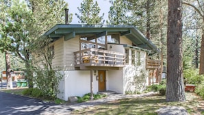 Un chalet doté d’un balcon, entouré d’arbres et bordé d’un sentier en pierre.