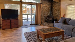Un salon avec une cheminée en pierre, un téléviseur posé sur un meuble en bois et un canapé gris.