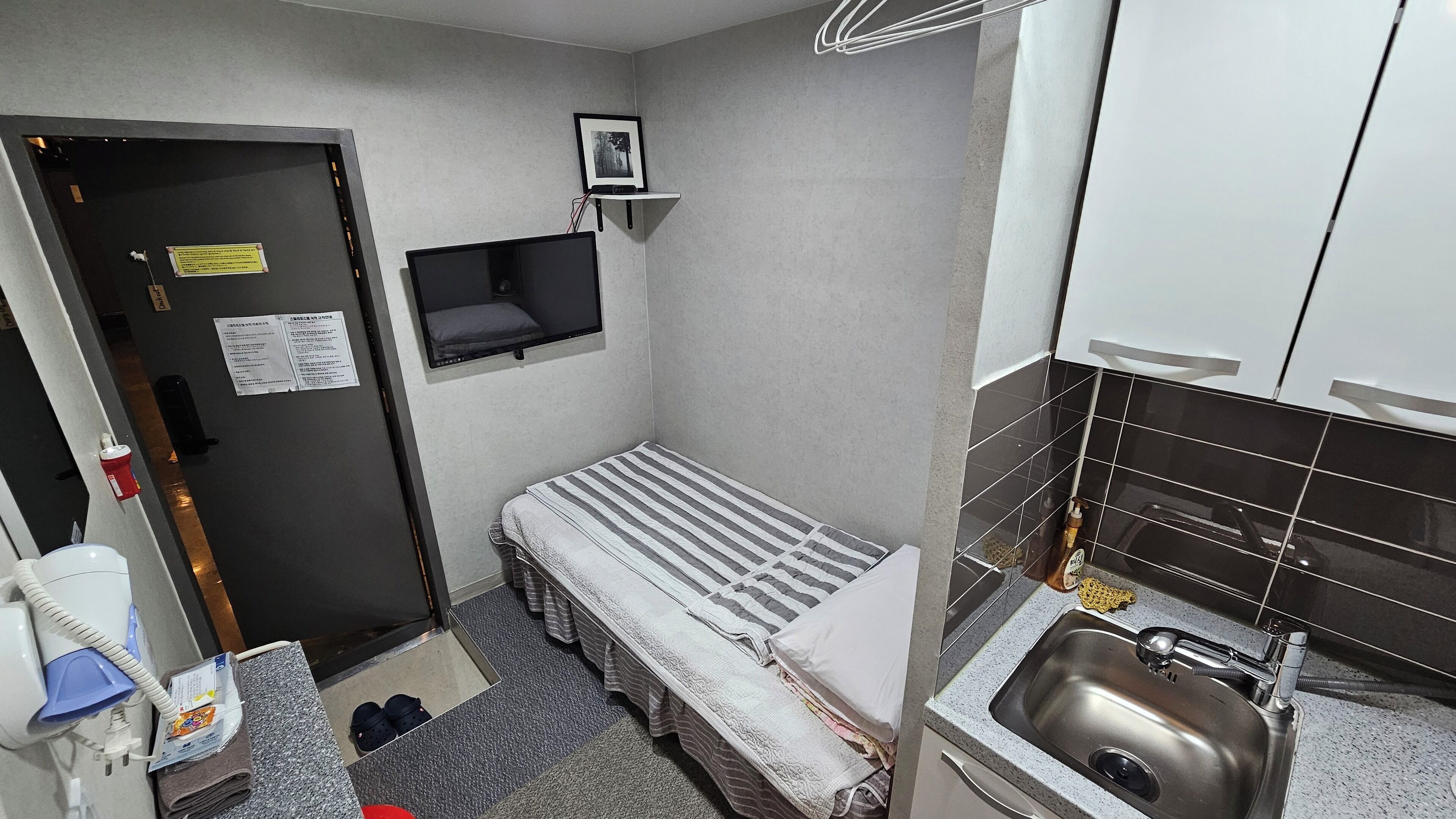 A compact hotel room with a bed, a small table, a sink, and a door.