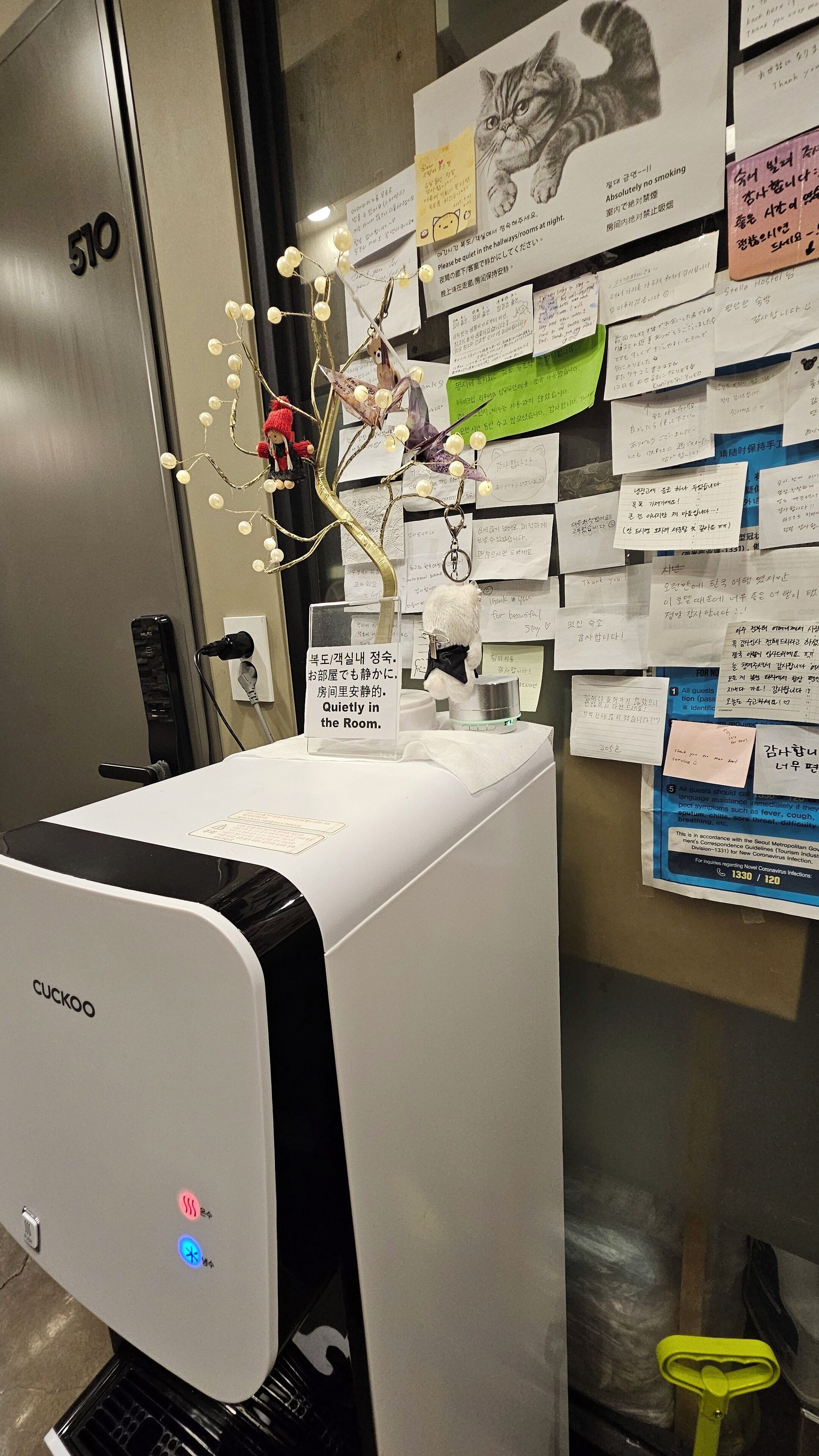 A room with a Cuckoo printer, a wall with various notes and a cat illustration, and a door labeled '510'.