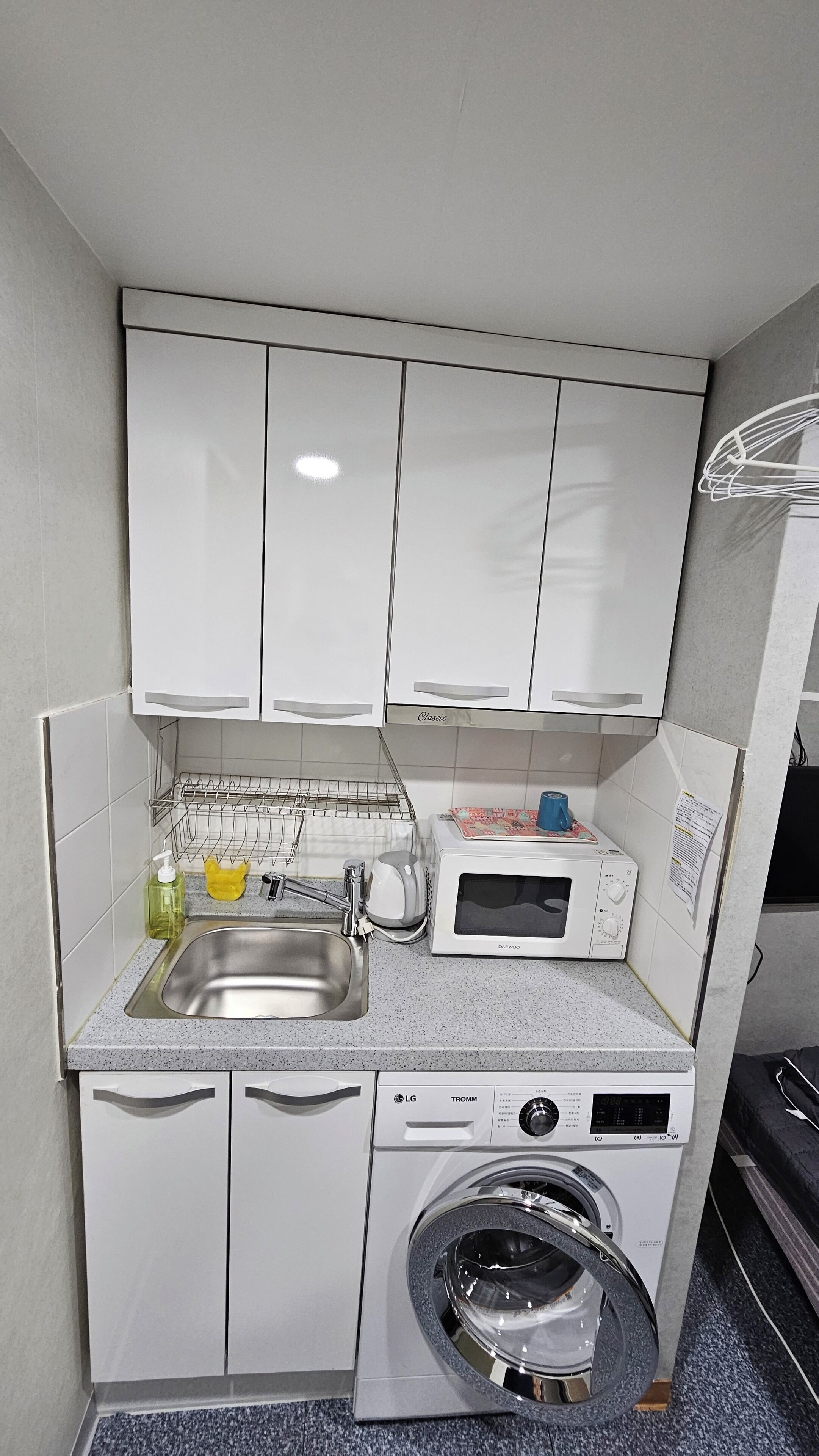A compact kitchen with a sink, a microwave, a dish rack, and a washing machine.
