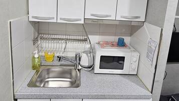 A compact kitchen with a sink, a microwave, a dish rack, and a washing machine.