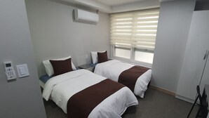 Ein Hotelzimmer mit zwei Betten, einem Kleiderschrank, einem Fenster mit Jalousien und einem Telefon an der Wand.