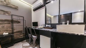 Habitación de hotel compacta con kitchenette, un espejo grande, un escritorio con computadora y un refrigerador pequeño.