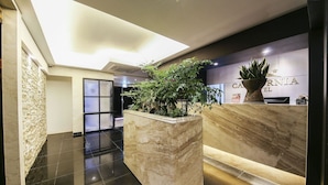 Un vestíbulo de hotel con mostrador de recepción, una gran planta en maceta, un muro decorativo y un diseño moderno de techo.