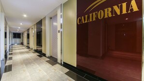 Un pasillo de hotel con un estampado de cuadros en el suelo, un cartel que dice 'California' a la derecha y un extintor a la izquierda.