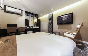Une chambre d’hôtel dotée d’un grand lit, d’un téléviseur à écran plat fixé au mur, d’un bureau avec une chaise, d’une petite table et d’un panneau décoratif mural.