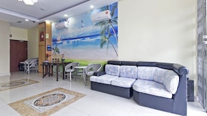 A modern living area with a sofa, dining table, chairs, and a mural of a beach scene. - Hotel Raja Bot (Kuala Lumpur)