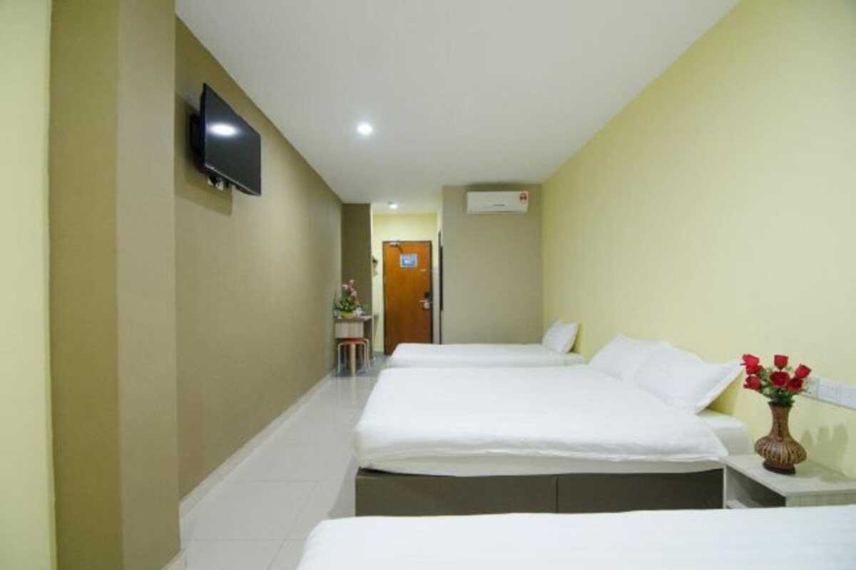 A hotel room with two beds, a TV mounted on the wall, a desk with a chair, and a vase with flowers.