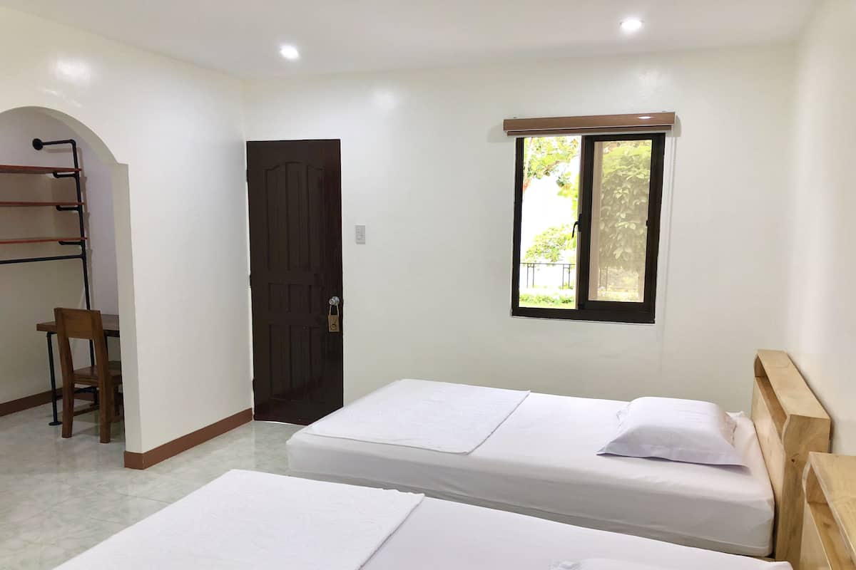 Une chambre avec deux lits, une chaise en bois, un bureau, une porte et une fenêtre donnant sur un paysage verdoyant.