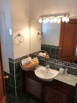 Un baño con lavamanos, espejo, toalleros y una cesta de toallas.